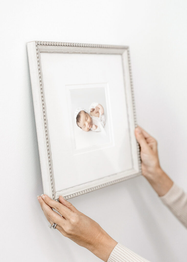 Hands hanging a framed newborn photoon the wall
